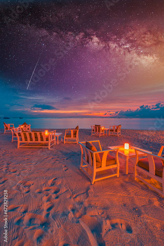 Outdoors restaurant table setting at tropical beach restaurant. Led light candles and wooden tables, chairs under beautiful sunset night sky, sea stars view. Luxury hotel or resort leisure restaurant