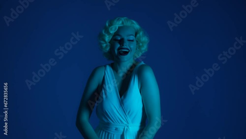 A woman in the image of poses under camera flashes, sends an air kiss. Woman in studio in pink and green neon light. photo