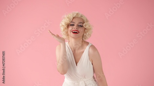 Portrait young woman in wig, white dress and with red lipstick on lips in studio on pink background. Woman looking like in studio on pink background.