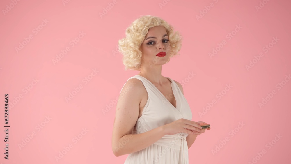 Side view of a bright woman in the image of . Woman holding a mirror in her hands in a studio on a pink background. Side view of a bright woman in the image of . Woman holding a mirror in her hands in a studio on a pink background.