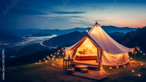 Luxury glamping camping tent with cozy accessories, light garlands and beautiful landscape at sunset. Warm cozy light inside camp tent. Millennial trend vacation destination. Staycation in mountain