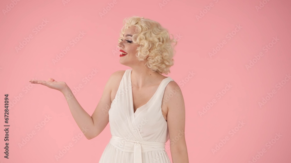 The woman points her hand to the side, recommending. Woman in the image of in the studio on a pink background. Advertising, promo, copy space.