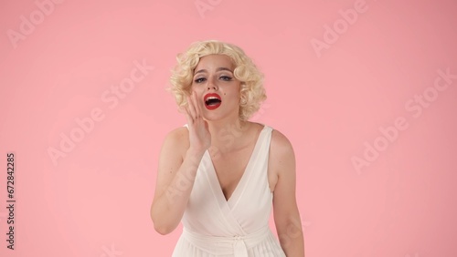 Woman putting her hand to her mouth that screams, calling someone. Woman in the look of in the studio on a pink background.