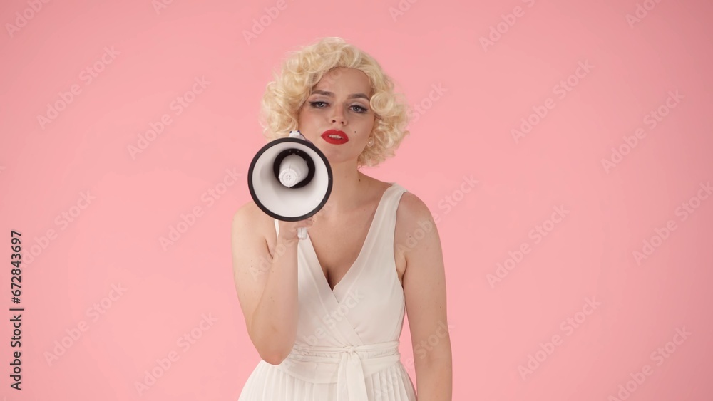 Obraz premium Woman in character of speaking into megaphone. Woman with colorful makeup, wig and white dress in studio on pink background. Sale, Black Friday. Copy space.