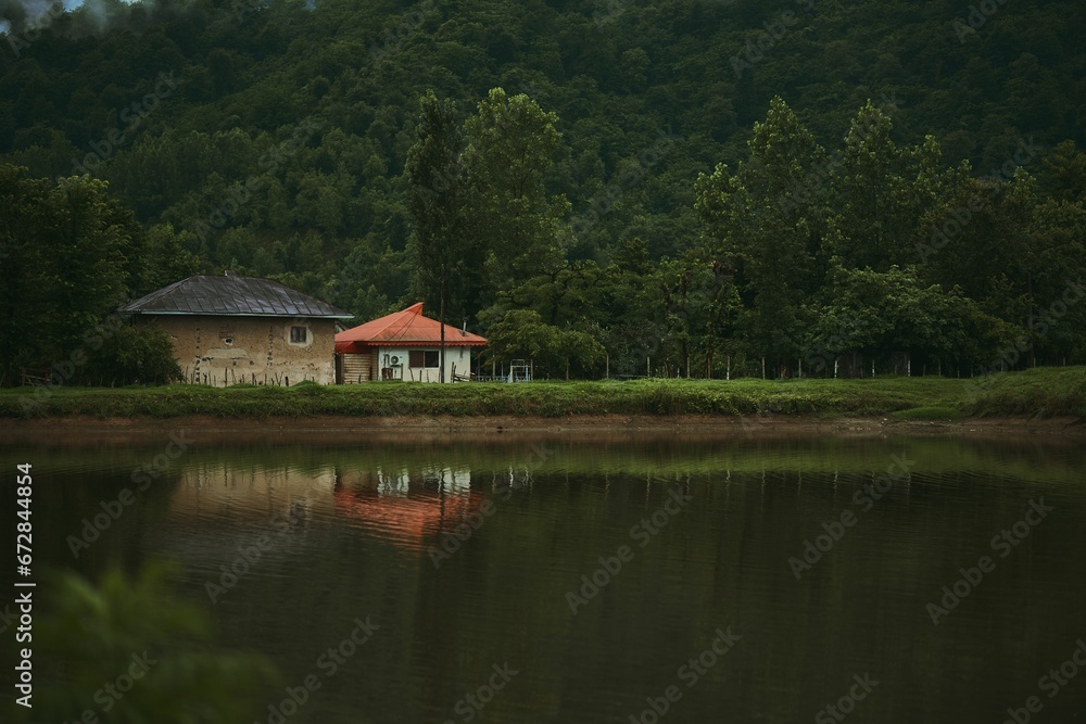 Scenic view of rural houses on the lakeside with lush woods in the background.