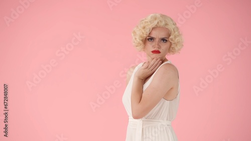 Side view of an offended young woman with pouting lips. Profile portrait of woman looking like , wearing white dress and white wig in studio on pink background. photo