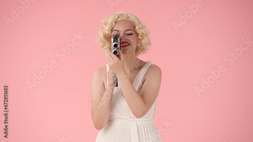 Woman using retro video camera close up. Woman looking like in studio on pink background.