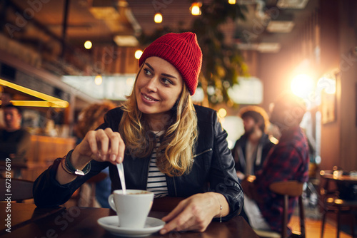 Attractive young woman stirring coffee at the cafe photo