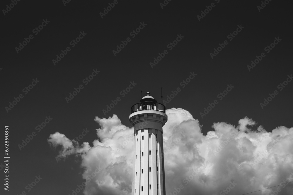 Monochromatic image of a small lighthouse, standing tall against a cloudy sky.