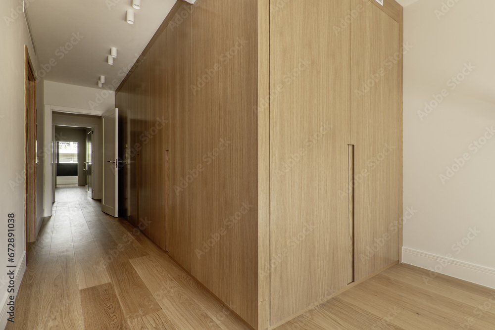 Beautiful contemporary designed room with a large custom-made wardrobe with white oak wooden doors with integrated structure in the wall and matching wooden floors Beautiful contemporary designed room with a large custom-made wardrobe with white oak wooden doors with integrated structure in the wall and matching wooden floors