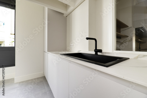 aundry room of a home with smooth white wooden furniture with a black synthetic sink with a faucet of the same color