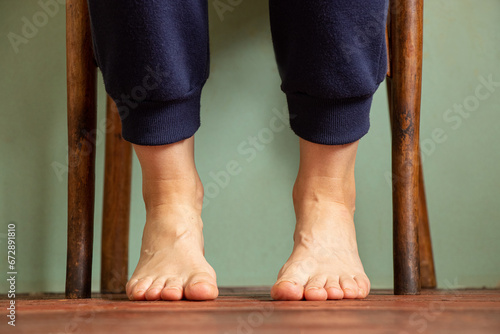 Female legs of a young girl who sits on a chair at home on a wooden old floor, bare feet on the floor