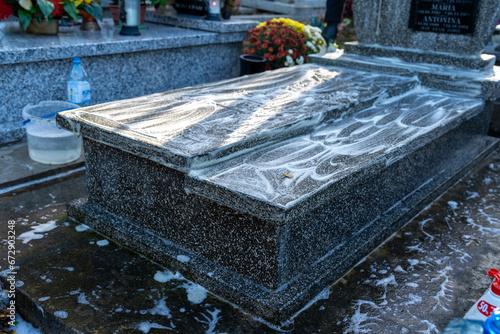 Preparing a grave for All Saints' Day celebrated on November 1st, a woman cleans and washes a marble tomb using a special cleaning solution, brush, cloth, and water. The tomb is clean.