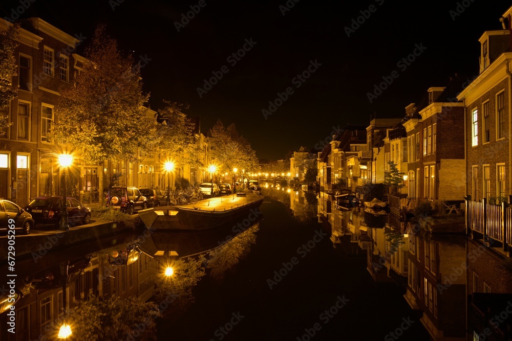 Fleet of boats in a canal in front of a picturesque row of houses at night: Leiden