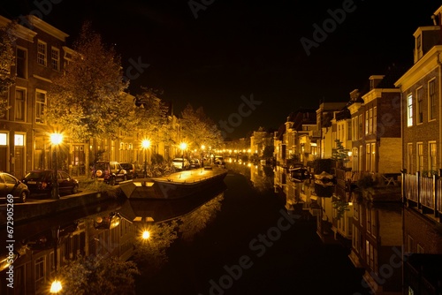 Fleet of boats in a canal in front of a picturesque row of houses at night  Leiden