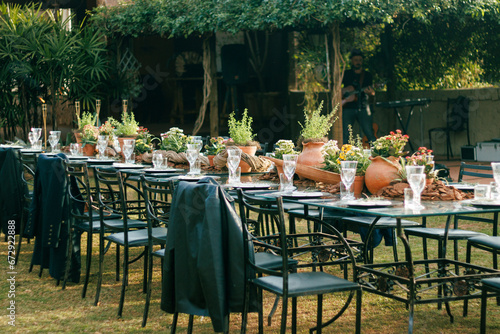 Outdoor dining setup for a sophisticated event featuring crystal glassware, polished plates, and a rustic wooden centerpiece surrounded by fresh potted herbs