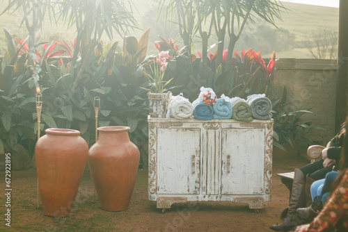 Antique cabinet with towels set against a backdrop of lush tropical plants and terracotta pots in an outdoor spa setting
