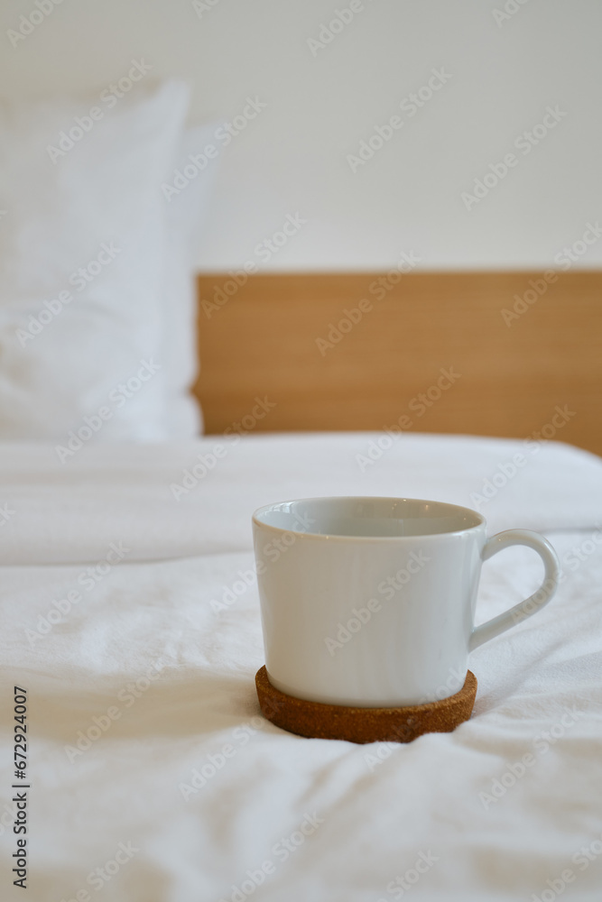 Fototapeta premium White cup with coffee or tea on the bed. Cozy morning photo. The concept is cozy and warm. Place for text