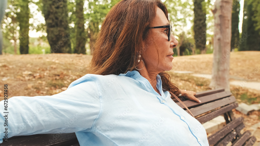 Close-up of beautiful retired woman with glasses having rest relaxing while sitting in the park Close-up of beautiful retired woman with glasses having rest relaxing while sitting in the park