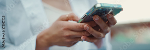 Closeup of young woman holds smartphone in her hands and scrolls through the news feed. Close-up of girl hand uses mobile phone outdoors