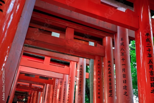 Array of red torii gates adorned with hieroglyphs near a temple