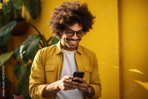 A cheerful young man smiles as he scrolls through social media on his mobile phone against a vibrant yellow background. Generative Ai.
