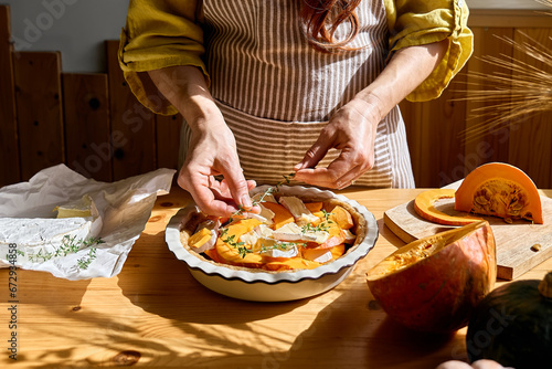 Autumn healthy eating. Woman preparing delicious seasonal tart with baked pumpkin, brie cheese and herbs.