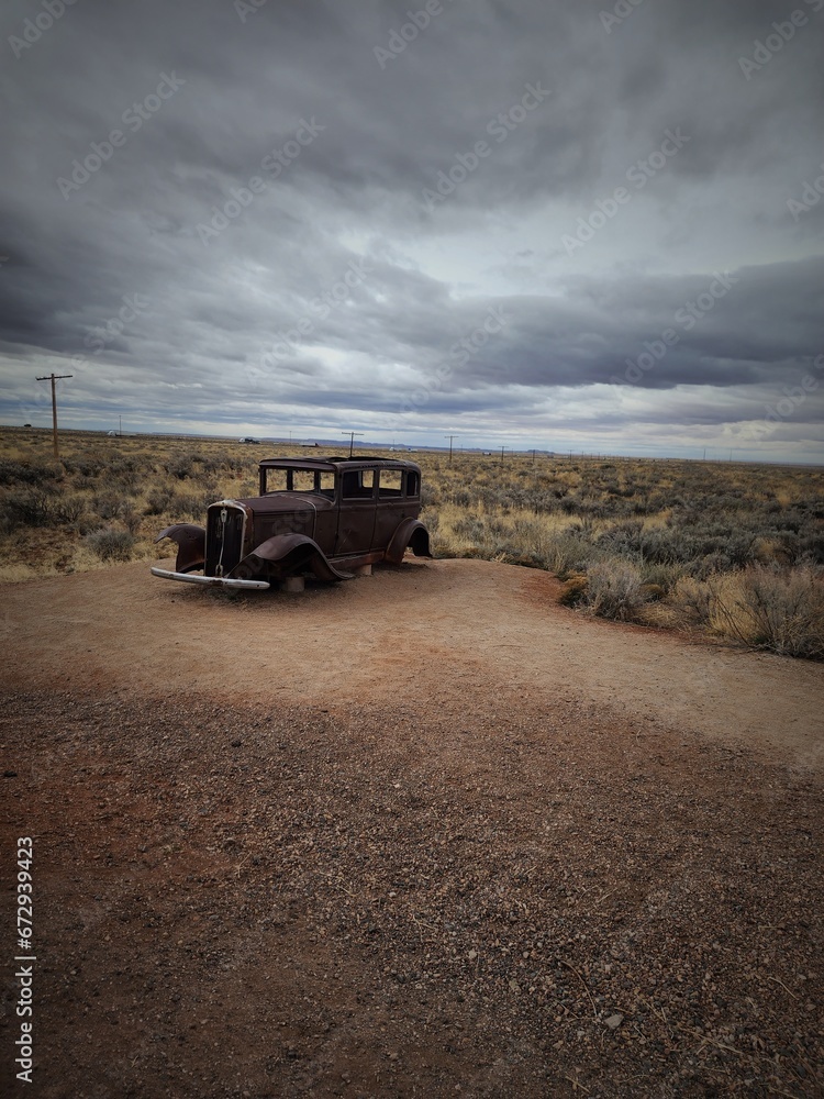 Obraz premium Vintage automobile parked along a scenic rural gravel road, with a backdrop of cloudy skies