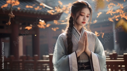 A beautiful Chinese woman in Hanfu prays with her hands together in an outdoor corridor, with a temple in the distance
