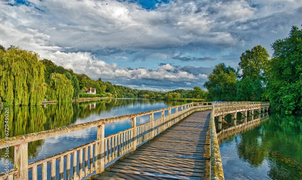 Wooden bridge over the River Thames surrounded by lush green trees