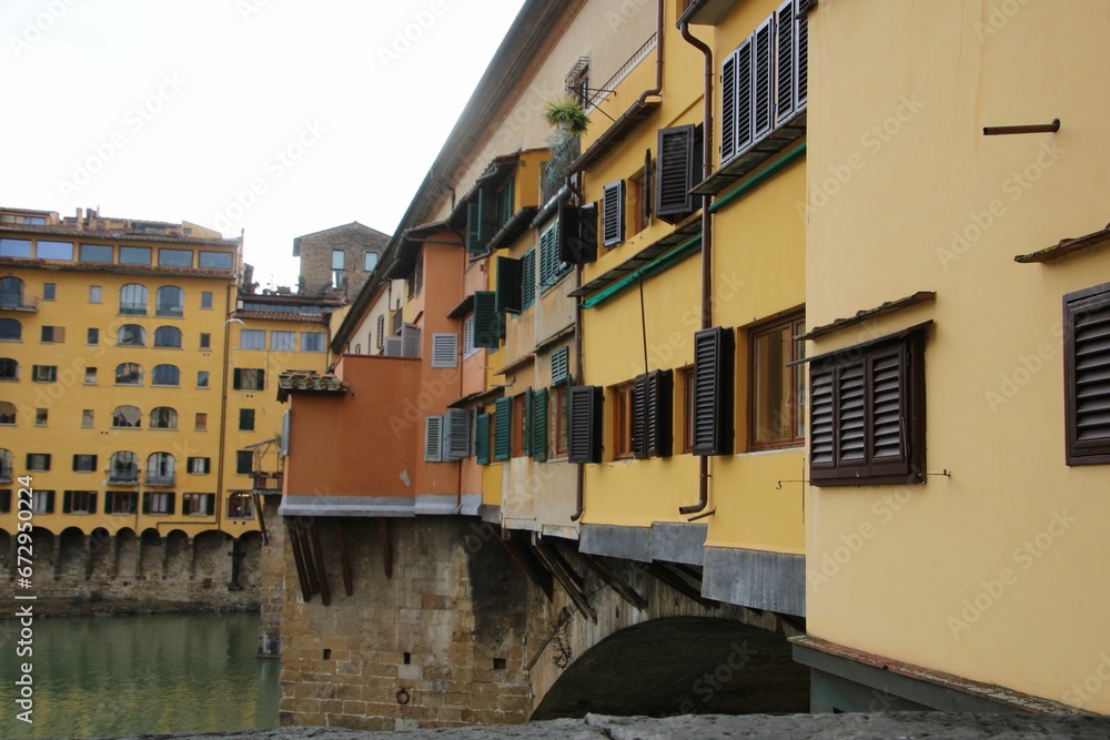 Old Bridge over water in Florence, Italy with urban buildings on the wall