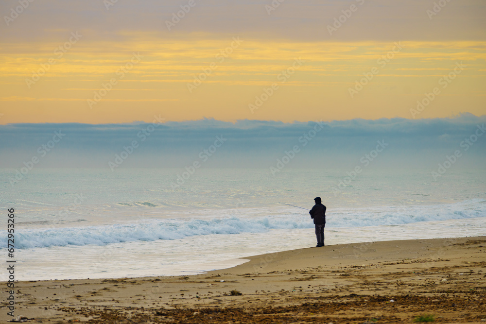Angler with fishing rod on sea shore Angler with fishing rod on sea shore