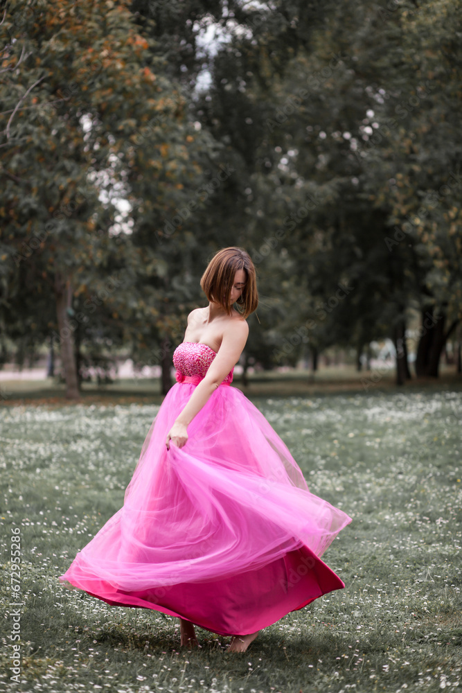 A beautiful ballerina in a pink dress dancing on the grass in the park A beautiful ballerina in a pink dress dancing on the grass in the park