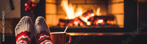 Feet in woolen socks by the Christmas fireplace. Person relaxing by the fire with a cup of hot drink. Close-up. Concept of winter vacations and Christmas. photo