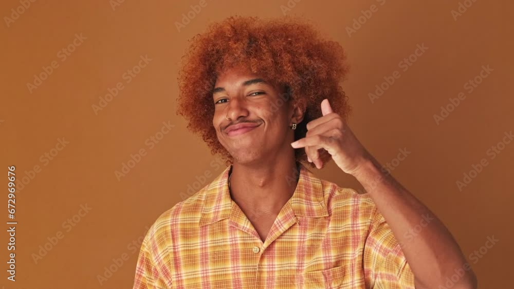Close up, guy shows call me phone hand sign gesture, isolated on brown background in studio Close up, guy shows call me phone hand sign gesture, isolated on brown background in studio