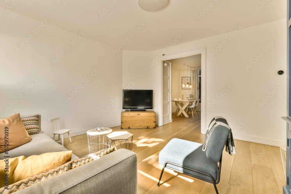 Fototapeta premium a living room with white walls and hardwood flooring, including a grey sofa set in the center of the room