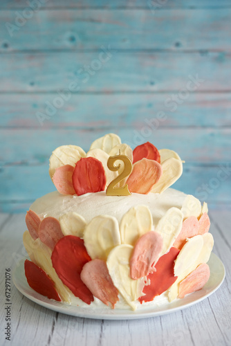Sponge cake with chocolate colorful petals stands on a plate on a wooden table