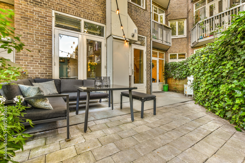 a patio with chairs, tables and plants on the side walk way to an outdoor living area that is surrounded by brick walls