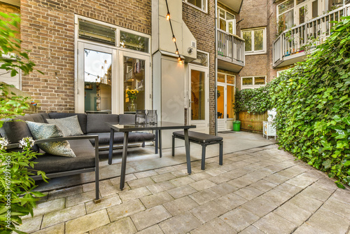a patio with chairs  tables and plants on the side walk way to an outdoor living area that is surrounded by brick walls