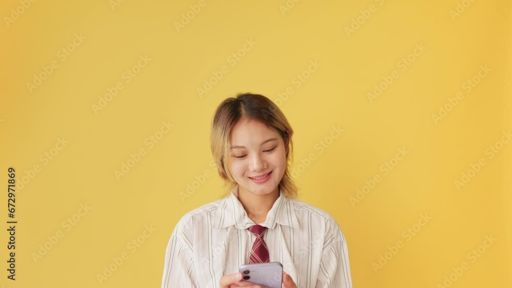 Smiling young woman using mobile phone isolated on yellow background in studio Smiling young woman using mobile phone isolated on yellow background in studio