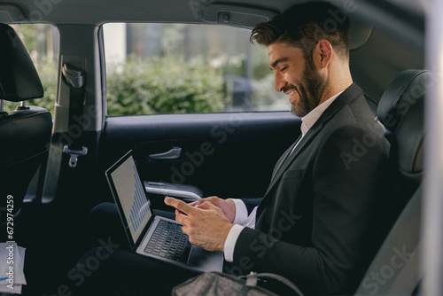 Handsome businessman in suit using personal computer and using mobile phone in taxi © Yaroslav Astakhov