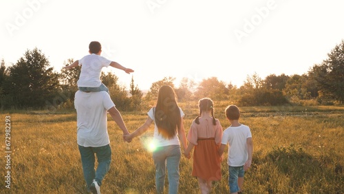 Strong friendly family with children walks raising hands across meadow at sunset