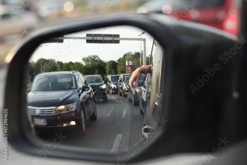 view in the car mirror: a small hand hanging from the car window on the background of a traffic jam © Indi