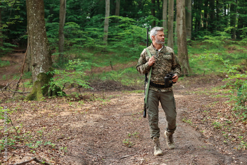 Man with hunting rifle and binoculars wearing camouflage in forest. Space for text
