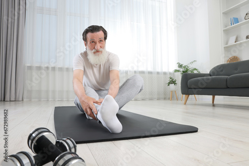 Senior man in sportswear stretching on fitness mat at home