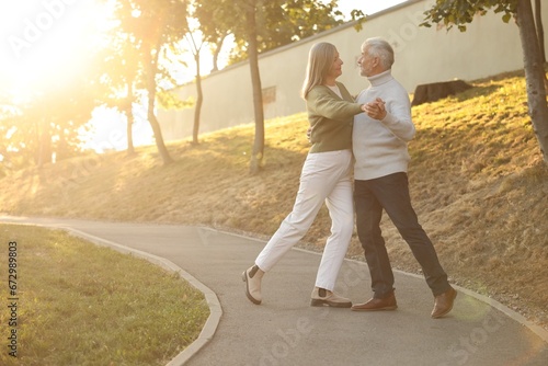 Affectionate senior couple dancing together outdoors at sunset, space for text