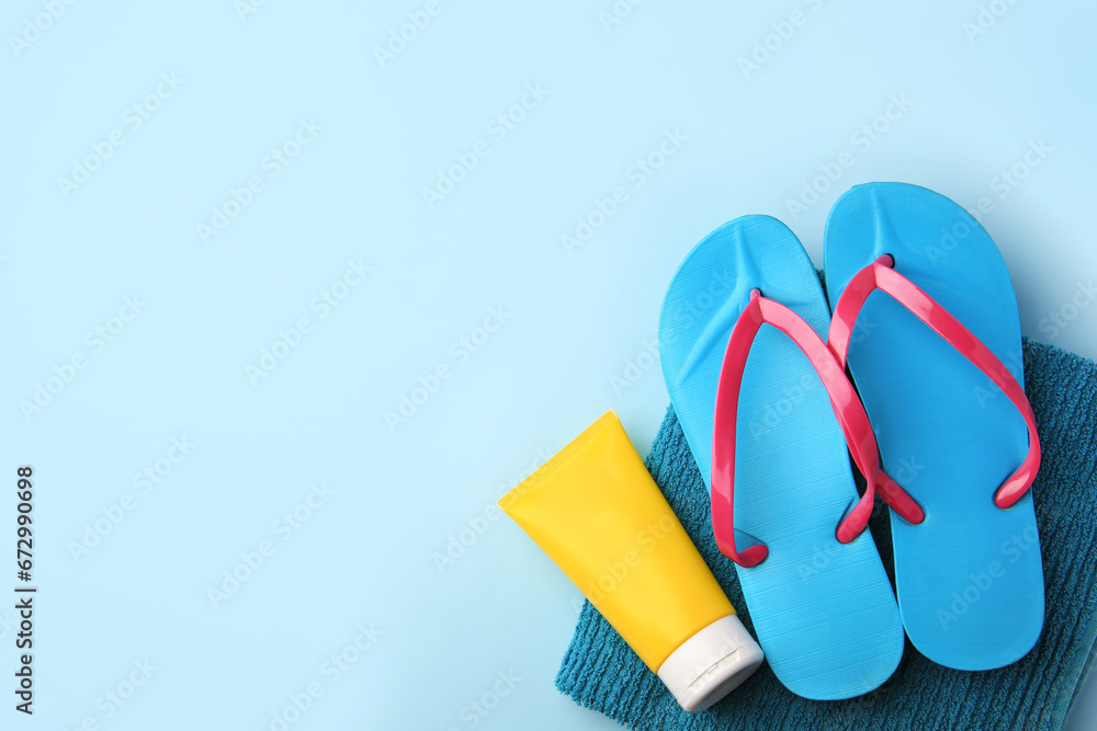 Towel, sunscreen and flip flops on light blue background, flat lay with space for text. Beach accessories Towel, sunscreen and flip flops on light blue background, flat lay with space for text. Beach accessories