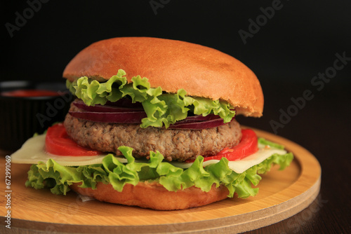 Tasty burger with vegetables, patty and cheese on wooden table, closeup