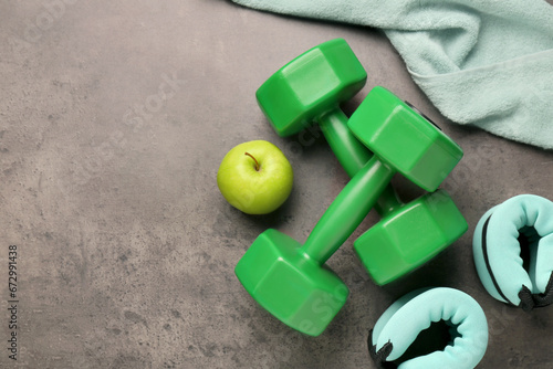 Dumbbells, apple, weights and towel on brown textured table, flat lay. Space for text