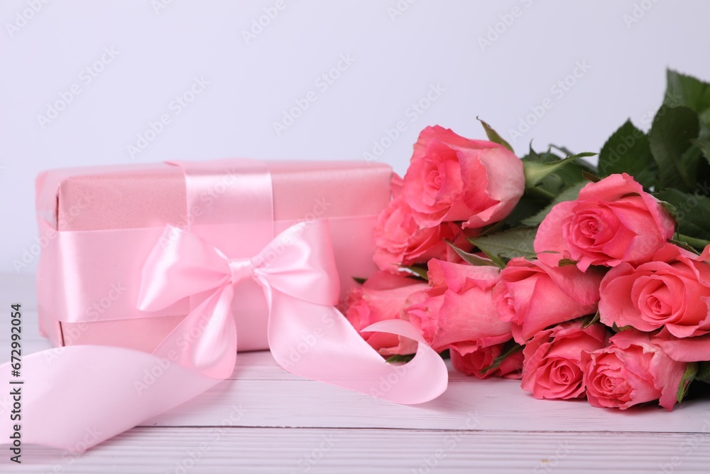 Gift box with pink bow and bouquet of beautiful roses on white wooden table, closeup